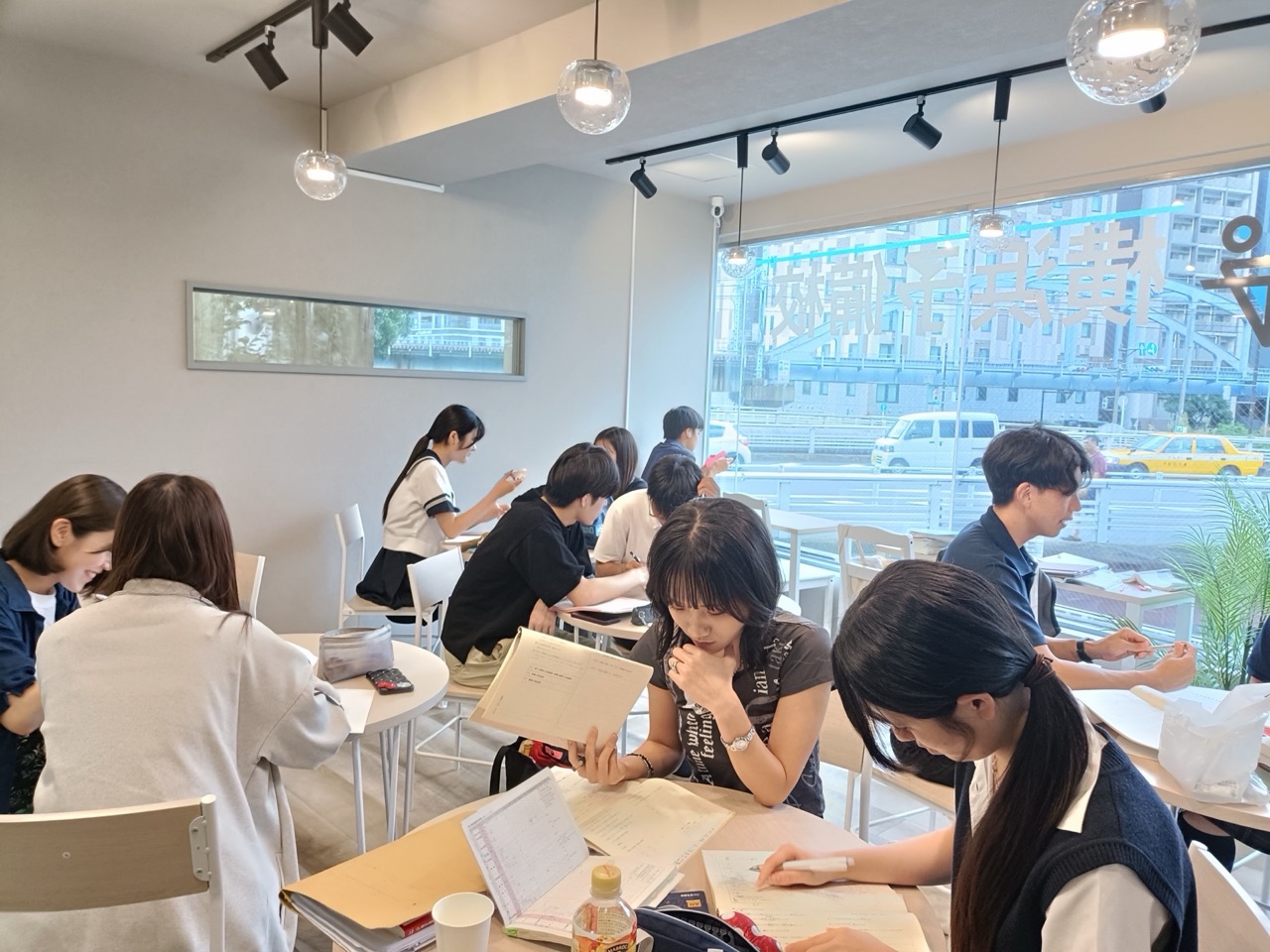 窓の外の橋を望む校舎で生徒と講師が学習する様子