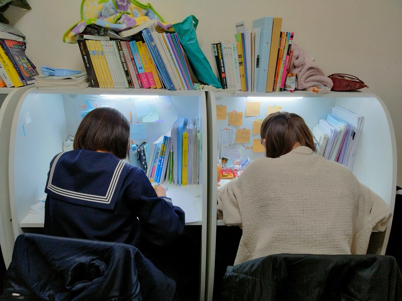 個別ブースで自習する生徒の後ろ姿と教材棚