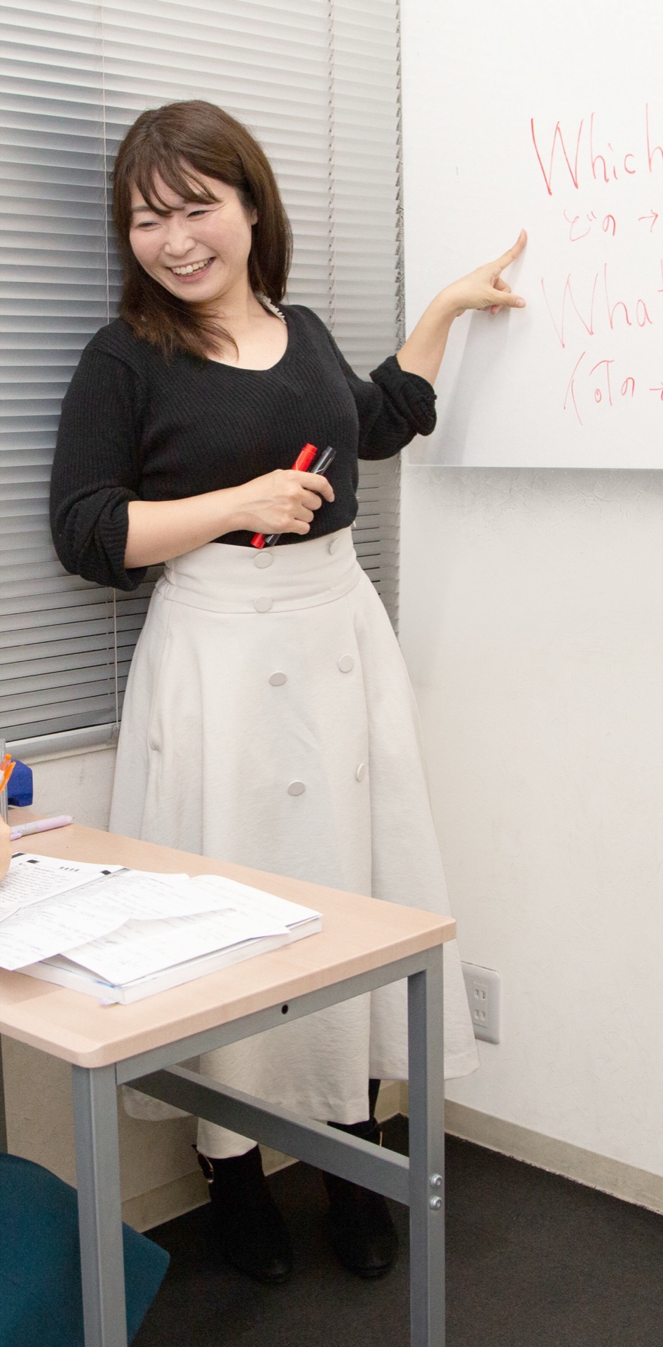 横浜予備校の個別授業風景。ホワイトボードに英作文を書いた女性講師が、机に向かう生徒に笑顔で英語を解説する様子