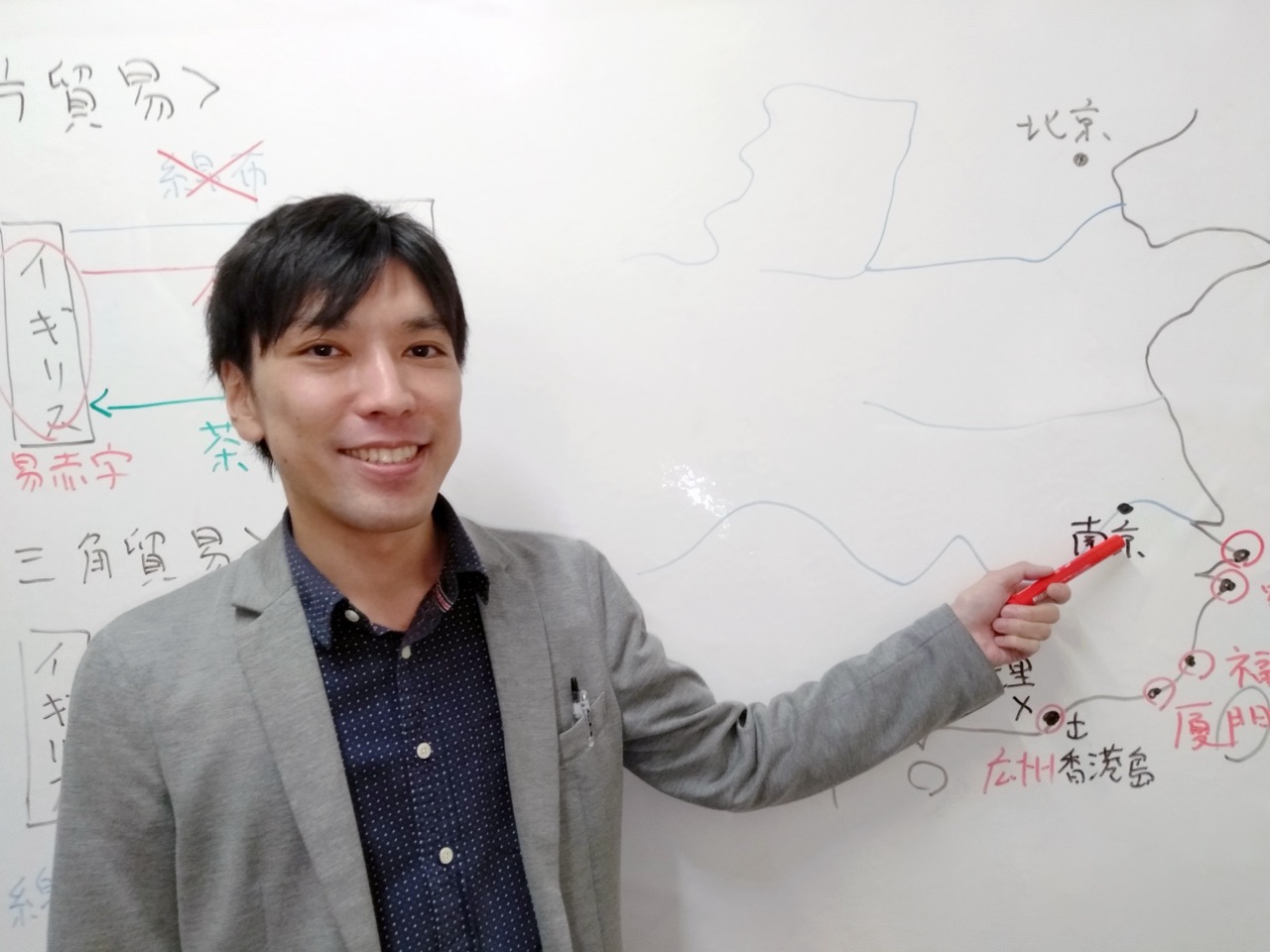 ホワイトボードに描かれた地図を指しながら笑顔で授業する講師