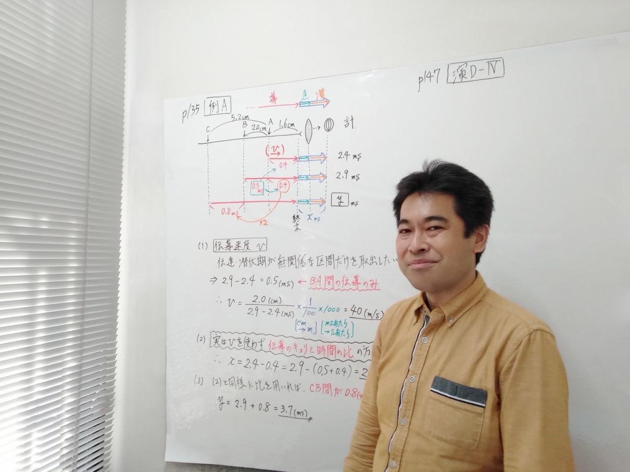 ホワイトボードの板書を背景に微笑む遠藤先生（講師・生物）